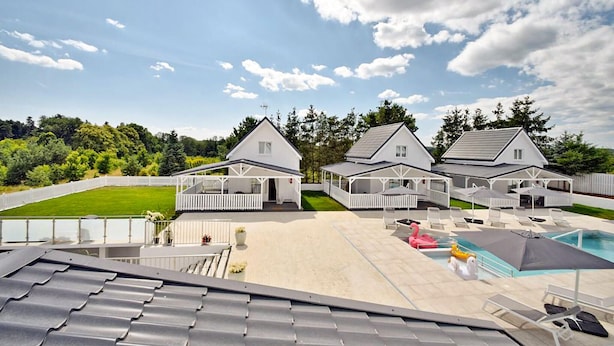 Ein Resort mit drei weißen Blockhütten, einem Poolbereich mit Liegestühlen und einem gepflegten Rasen.