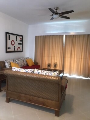 A living room with a sofa, a ceiling fan, a framed abstract artwork, and a window with curtains.
