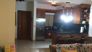 A living room with a sofa and a television. There is a kitchen in the background with wooden cabinets and a refrigerator. - Caribbean style villa directly on the beach (Cabarete)