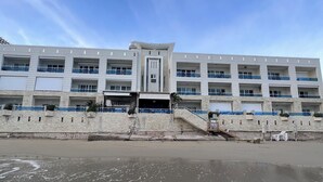 A multi-story building with a central entrance, balconies, and a beach in the foreground. - Caribbean style villa directly on the beach (Cabarete)