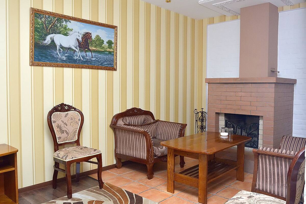 A room with striped wallpaper, a fireplace, a wooden table, and two upholstered chairs.
