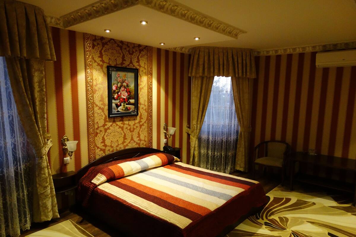 A hotel room with a large bed, striped curtains, a painting on the wall, and a desk with a chair.