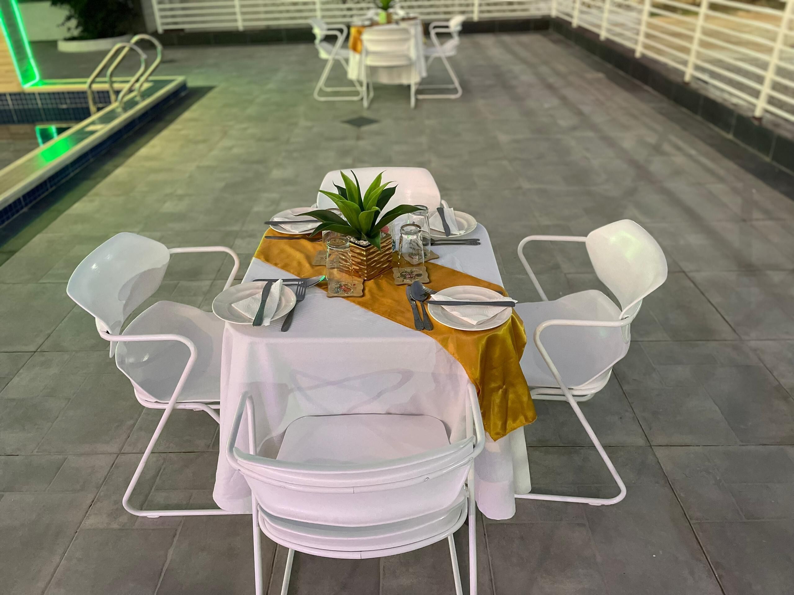 Comedor con una mesa dispuesta para cuatro personas, sillas blancas y mantel amarillo.