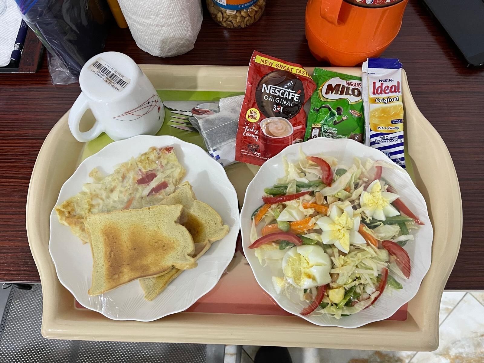 En bakke med morgenmadsprodukter, heriblandt ristet brød, en salat samt Nescafe og Milo.