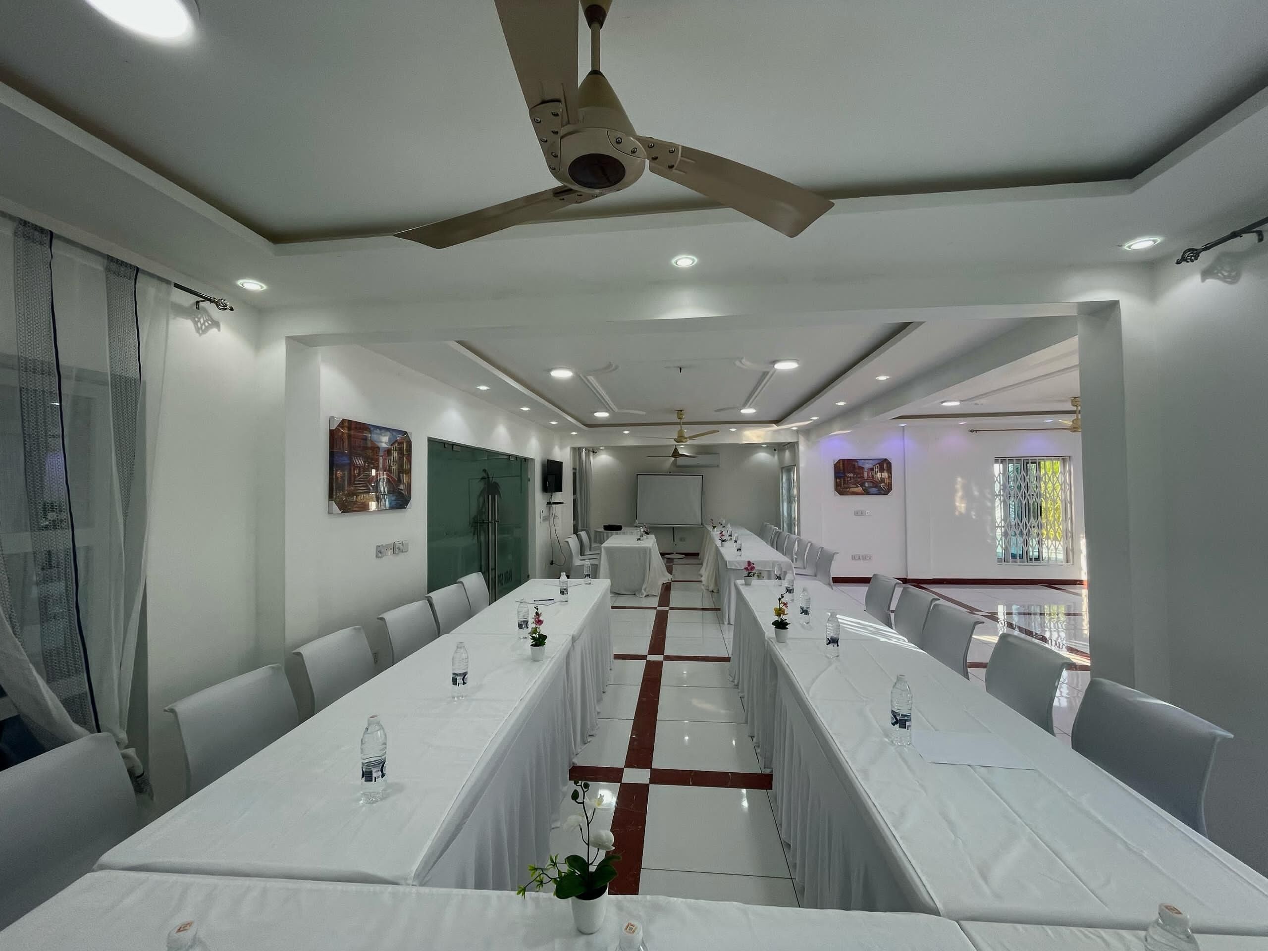A conference room with long tables, ceiling fans, and recessed lighting.
