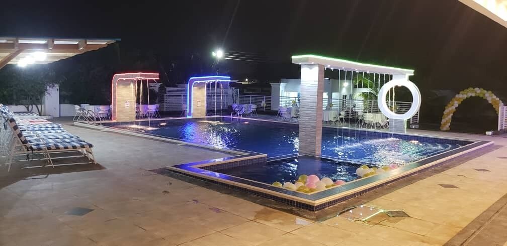 Zona de piscina amb una font, mobiliari i una zona coberta amb un llum circular.