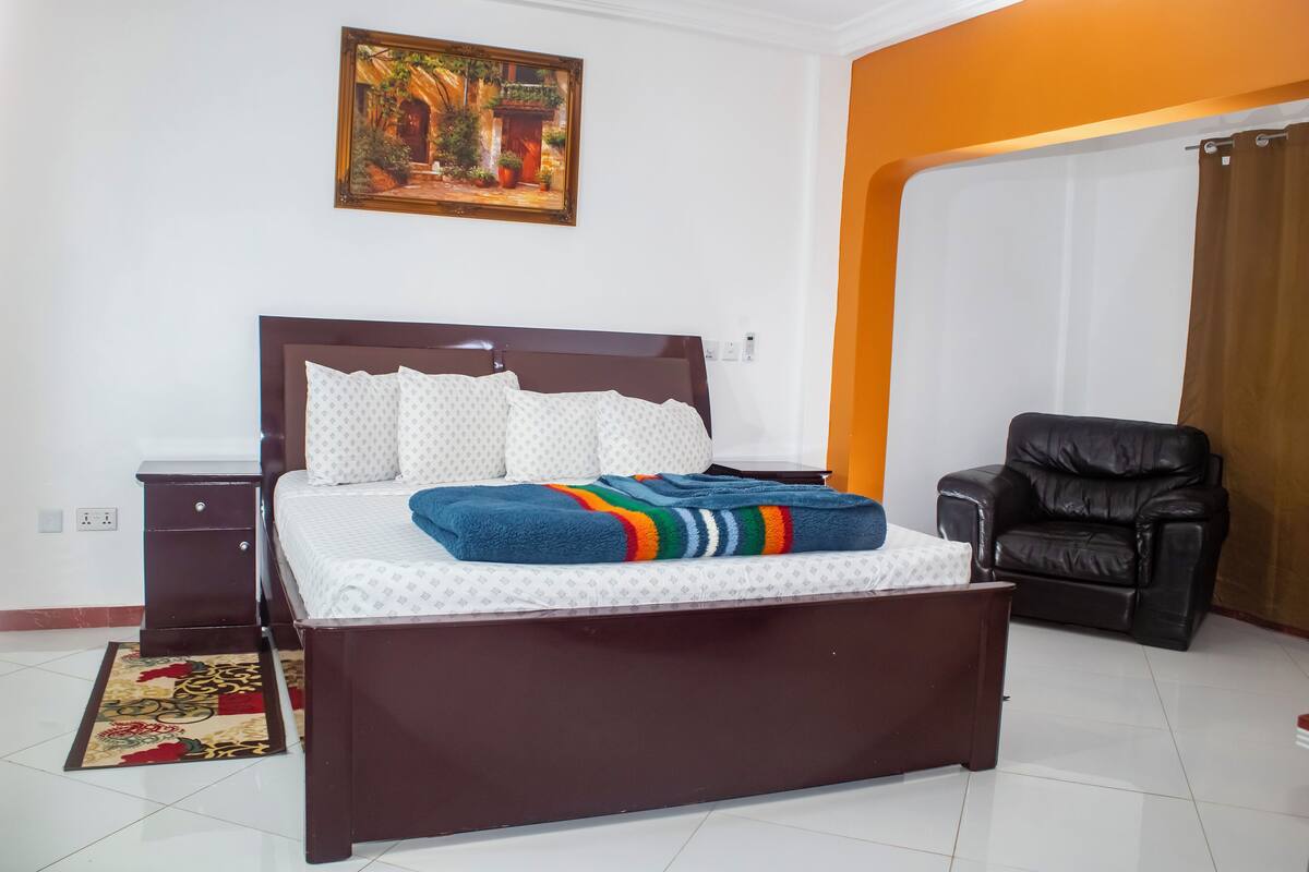 A bedroom with a bed, a nightstand, a chair, and a painting on the wall.
