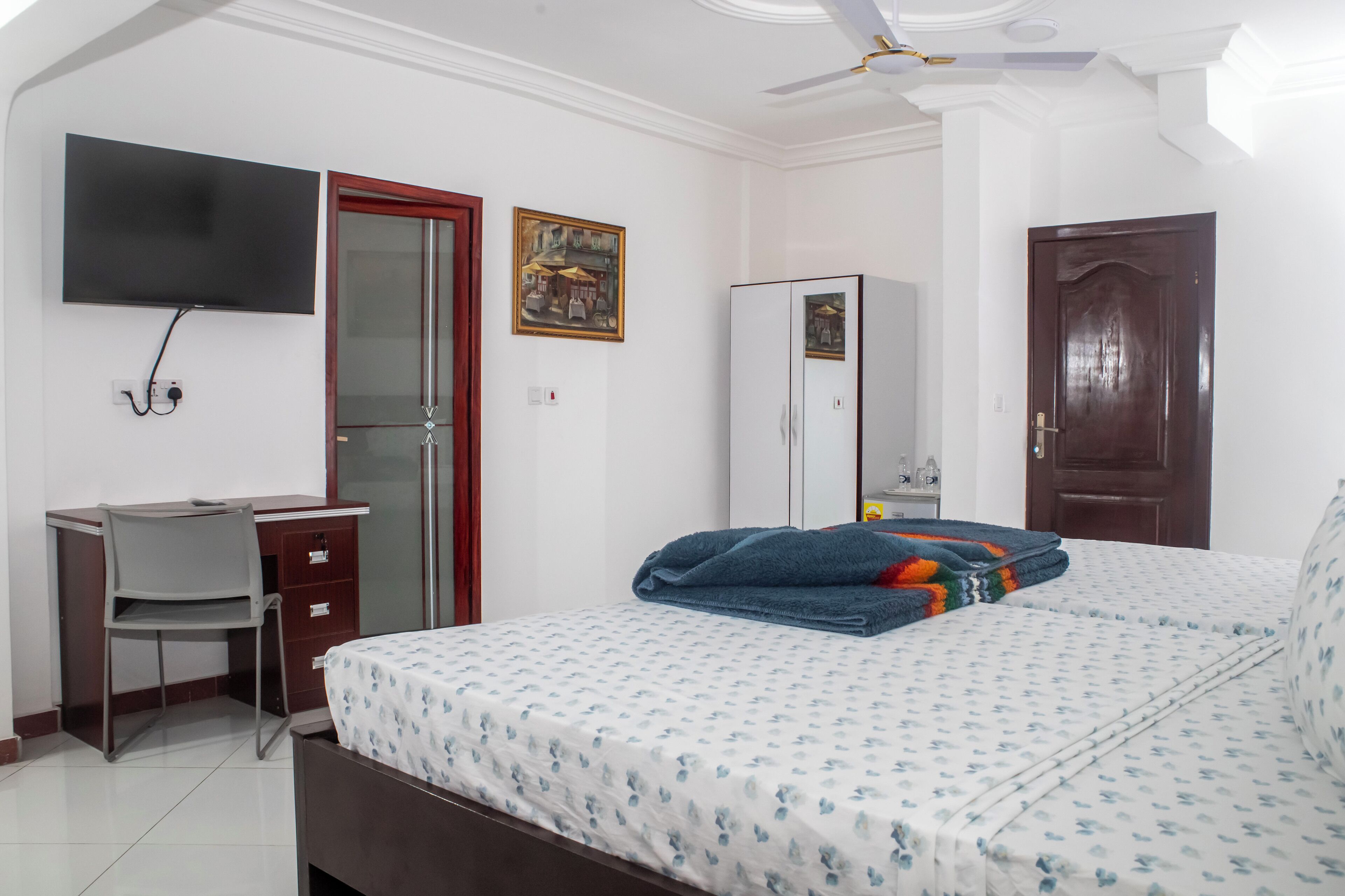 A bedroom with a bed, a desk, a chair, a wardrobe, a television, and a door.