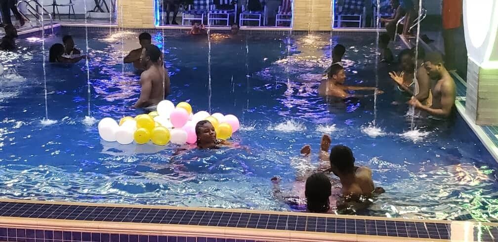 Une zone de piscine où se trouvent plusieurs personnes dans l’eau, dont certaines ont des ballons.