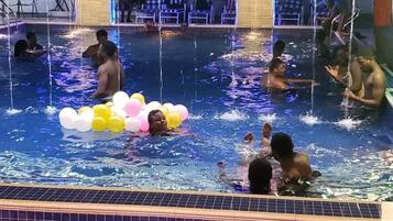 Une zone de piscine où se trouvent plusieurs personnes dans l’eau, dont certaines ont des ballons.