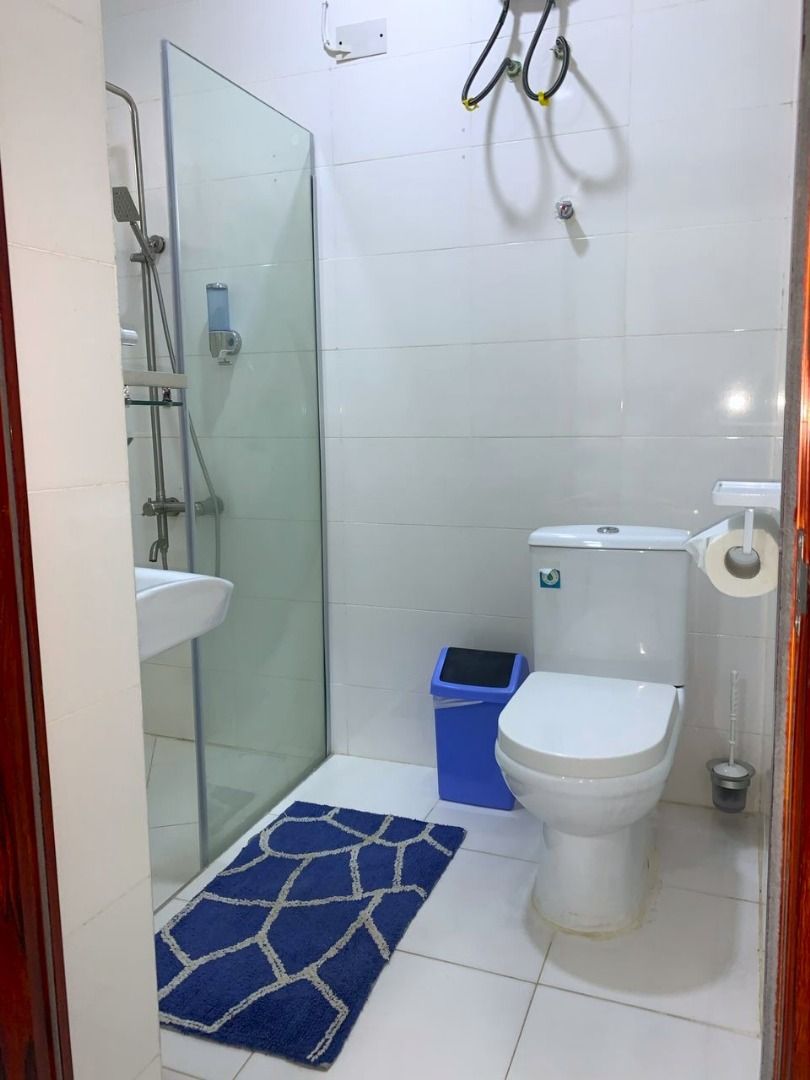 A small bathroom with a glass shower enclosure, a white toilet, a blue trash bin, and a white sink.