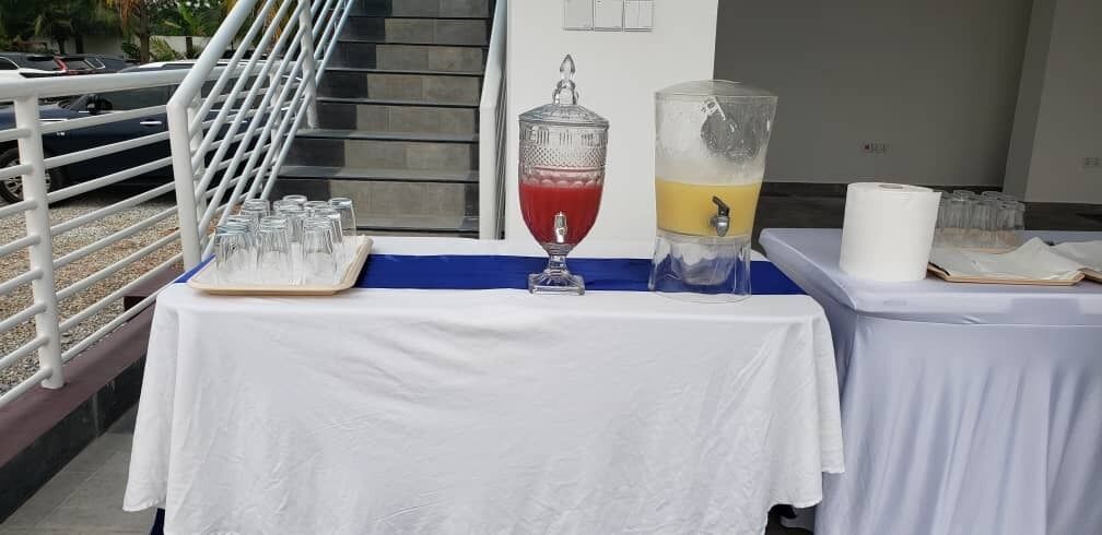 Une table avec un distributeur de boissons, des verres et un plateau de verres.