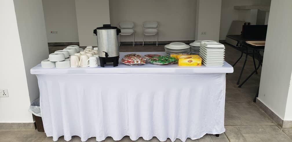 Ein reichhaltiges Buffet mit weißem Tischtuch, Tellern, Tassen und einer Kaffeekanne.