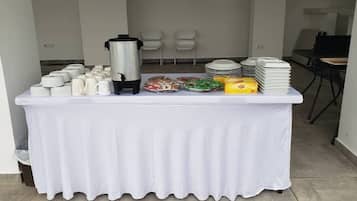 A buffet table with white tablecloth, plates, cups, and a coffee pot.