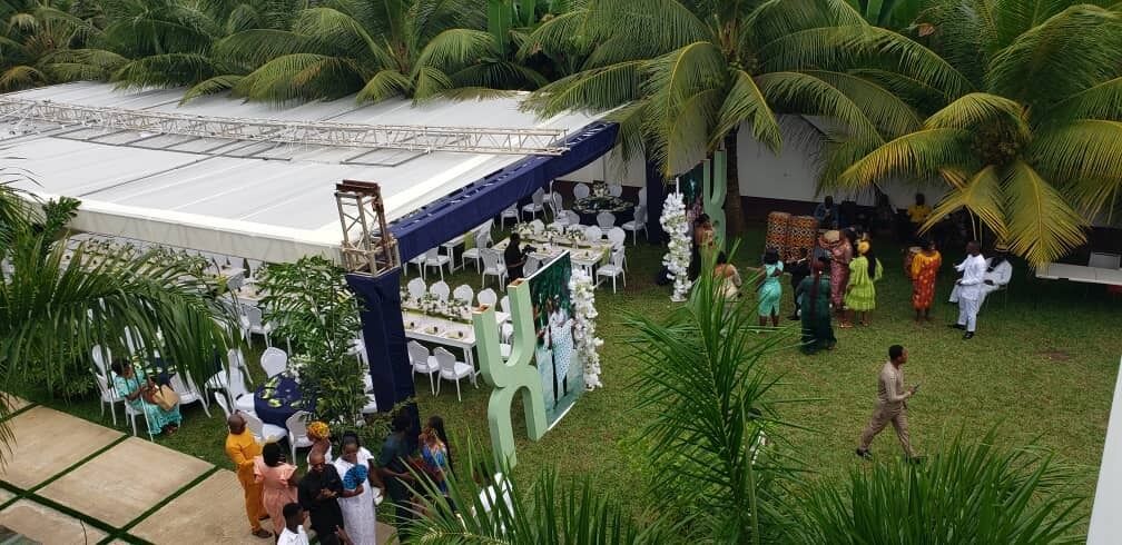 An outdoor event with a covered stage, seating, and palm trees.
