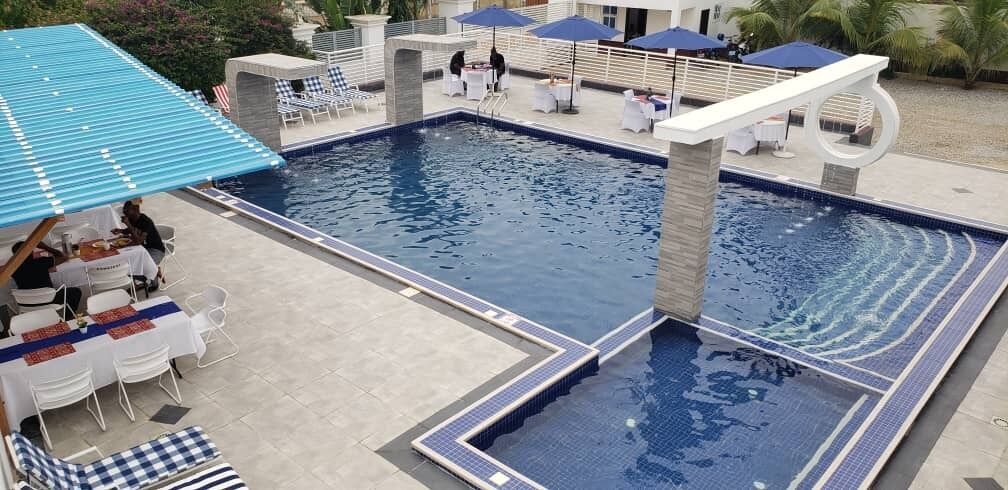 A swimming pool with a tiled deck area, lounge chairs, and tables.