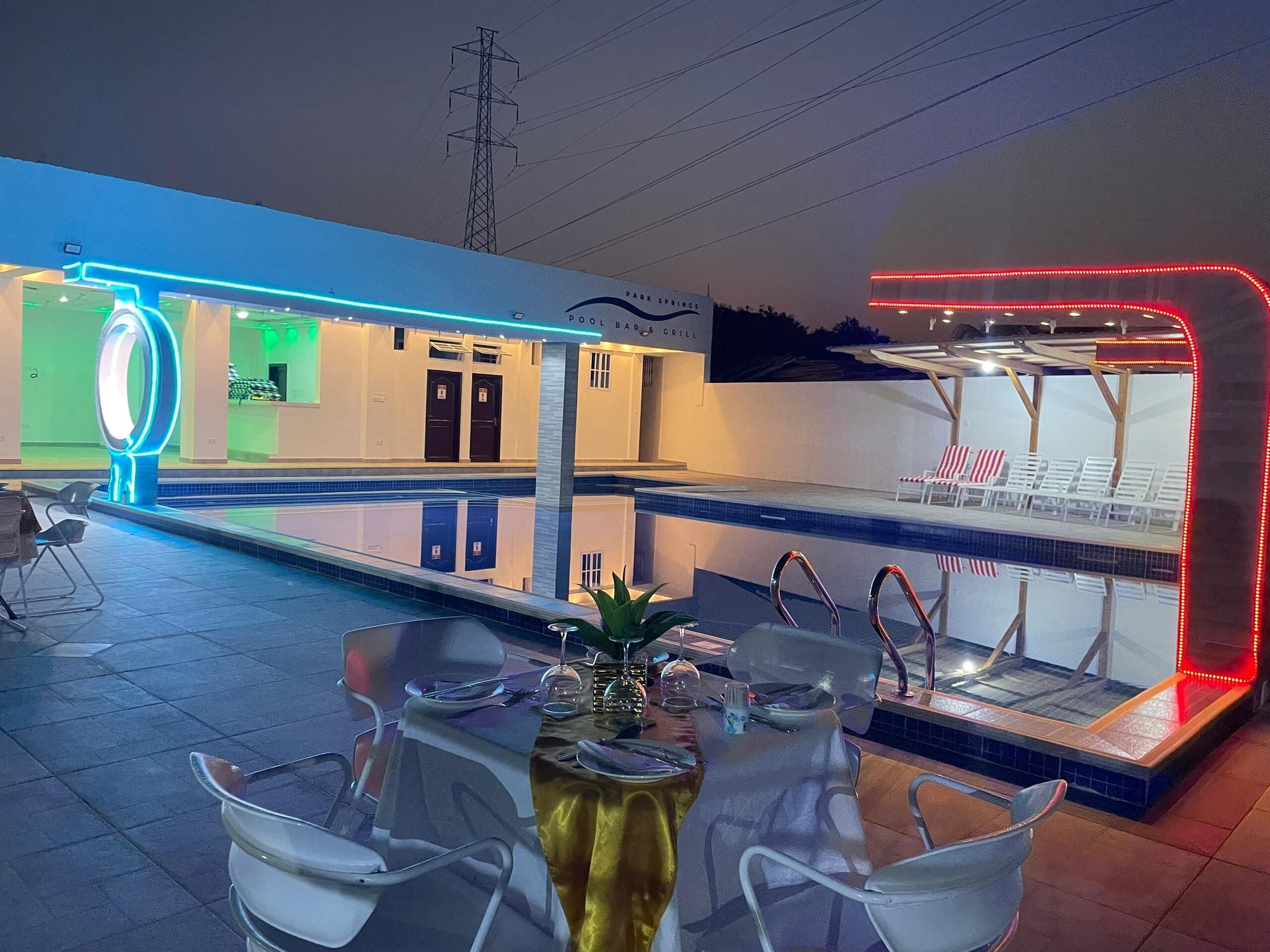 A pool area with a dining setup, including a table with chairs and a poolside bar.