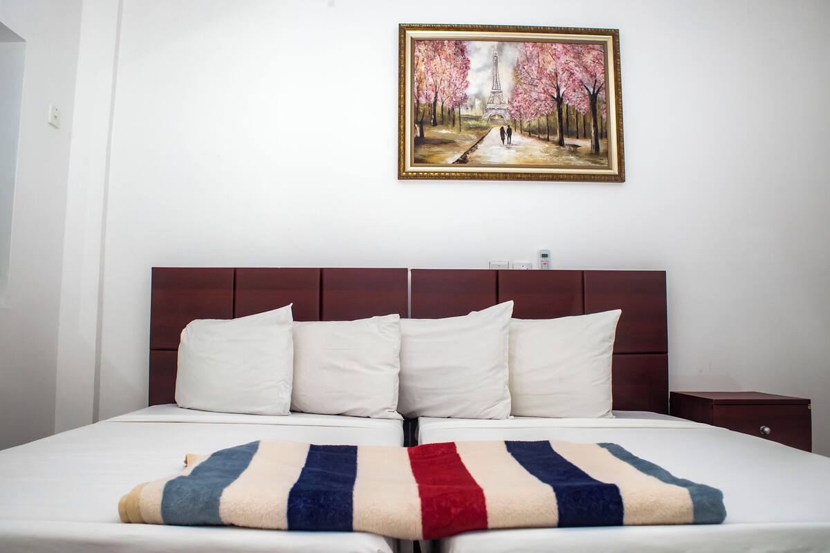 A double bed with a striped blanket, a wooden headboard, and a painting of a park scene above it.