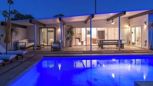 Et moderne poolområde med pool, liggestole og et overdækket siddeområde.