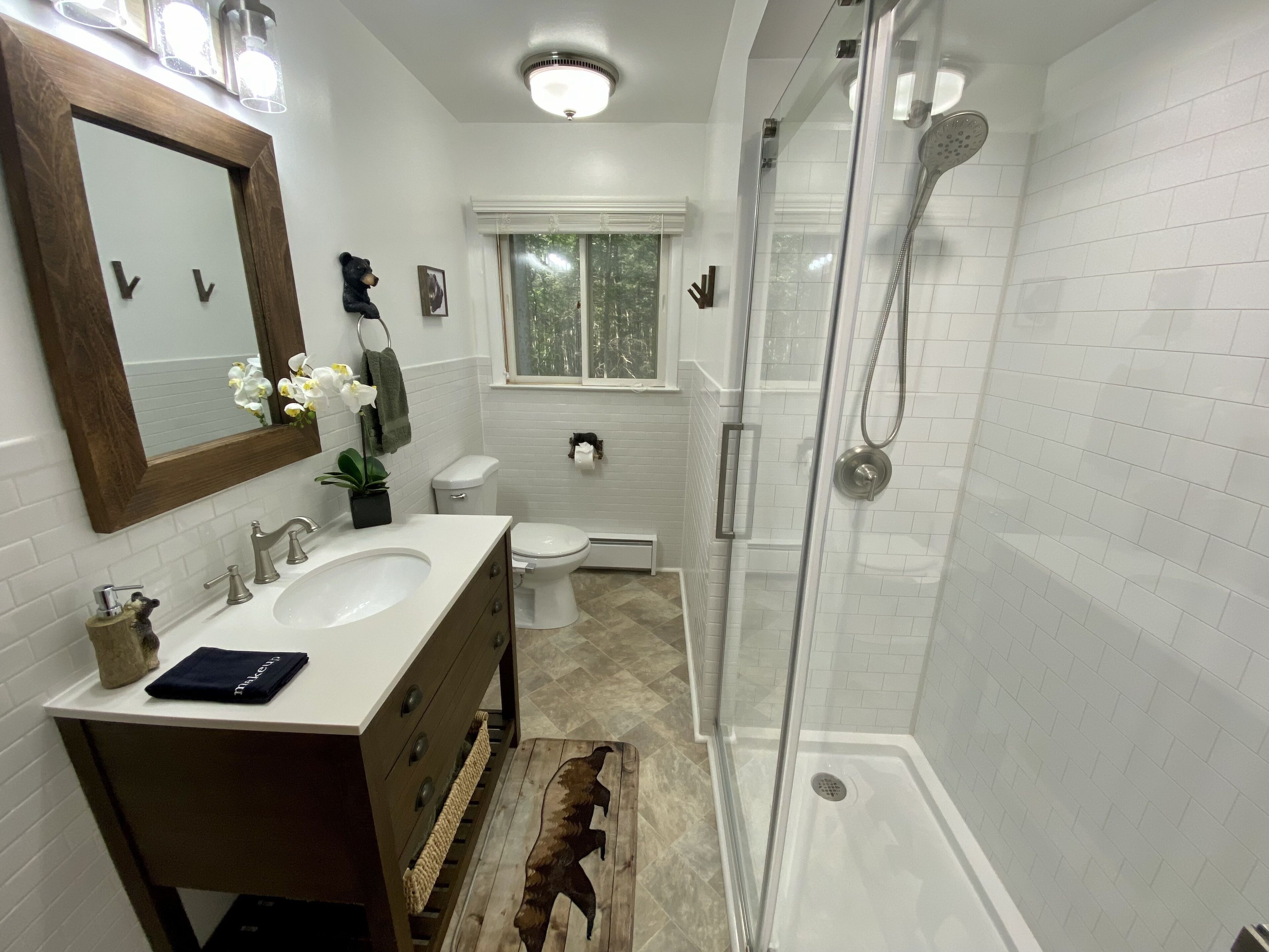 Une salle de bain moderne dotée d’un meuble-lavabo à deux vasques, d’une douche à parois de verre et d’une fenêtre laissant entrer la lumière naturelle.