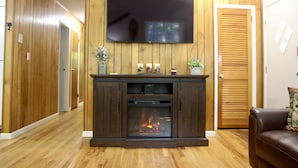 A living room with a fireplace, a television mounted above it, and a wooden door. - Enjoy the Lower Catskills (Woodridge)