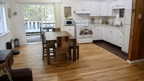 A spacious kitchen with wooden flooring, white cabinets, a microwave, stove, and a dining area with a table and chairs. - Enjoy the Lower Catskills (Woodridge)