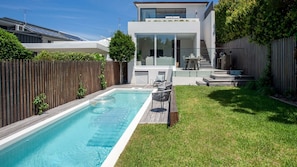 A modern house with a swimming pool, a wooden deck, and a patio with outdoor furniture.