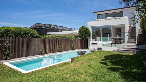 A modern house with a swimming pool, a wooden fence, and a well-maintained lawn.