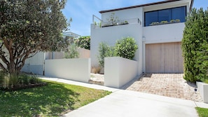 A modern two-story house with a flat roof, a large garage door, and a well-maintained garden with various plants and a tree.