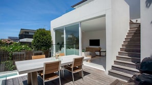 A modern outdoor dining area with a wooden deck, a glass-enclosed patio, and a staircase leading to an upper level.