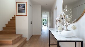 A modern hallway with a wooden staircase, a white console table with decorative items, and a large mirror on the wall. - Palatial 4 bedroom poolside home with tranquil views  (Clovelly)