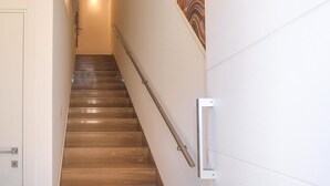 A wooden staircase with a handrail, a light fixture at the top, and a wall-mounted light switch. - Lovely apartment in Pozzallo with WiFi (Pozzallo)