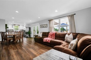 Una sala de estar moderna con un sofá de cuero marrón, una mesa de comedor de madera y una mesa de centro blanca.