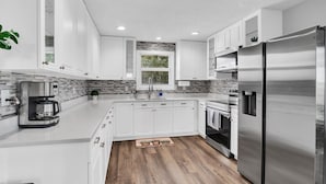 A modern kitchen with white cabinets, a stainless steel refrigerator, and a built-in oven. - Modern farmhouse cottage (Okeechobee)