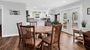 A modern kitchen with white cabinets, a stainless steel refrigerator, and a dining area with wooden chairs and a round table. - Modern farmhouse cottage (Okeechobee)