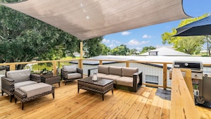 A wooden deck with outdoor furniture, a grill, and a view of trees and buildings. - Modern farmhouse cottage (Okeechobee)