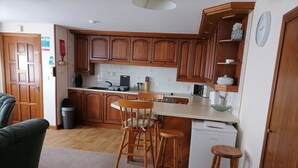 Una cocina compacta con armarios de madera, una mesa de comedor con sillas, un refrigerador pequeño y un microondas.