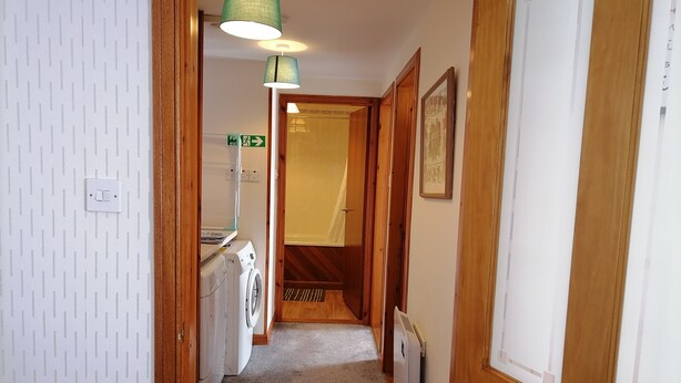 Un pasillo estrecho con lavadora, un radiador y una puerta que da a otra habitación.