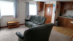 Una sala de estar con un sofá de cuero, un banco de madera y una zona de cocina con armarios de madera y un lavabo.