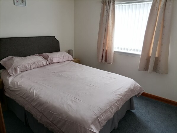 A neatly made bed with a headboard, a bedside table with a lamp, and a window with curtains. - Impeccable 2-bed Flat in Wick (Wick)