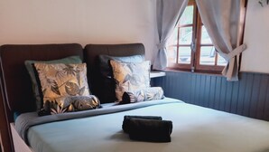Un dormitorio con cama, almohadas, una mesita de noche y una ventana con cortinas.