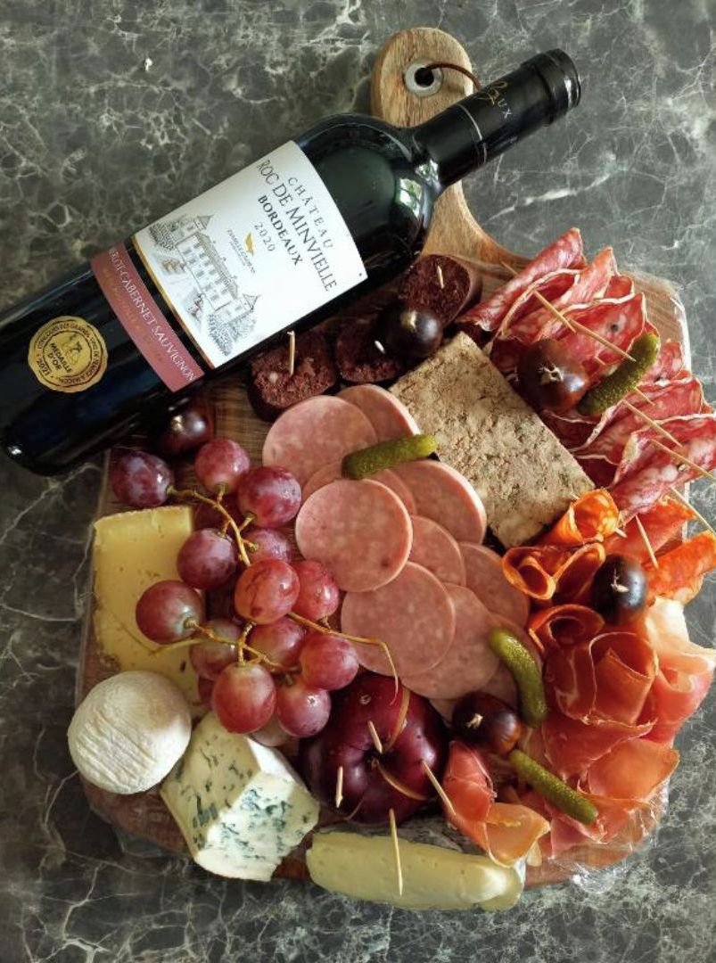Een charcuterieplank met diverse vleessoorten, kazen en druiven, vergezeld van een fles wijn.