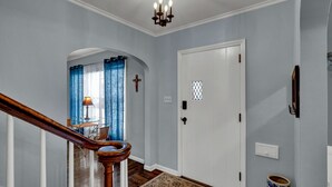 Un couloir avec un escalier en bois, une porte blanche et un tapis à motifs.