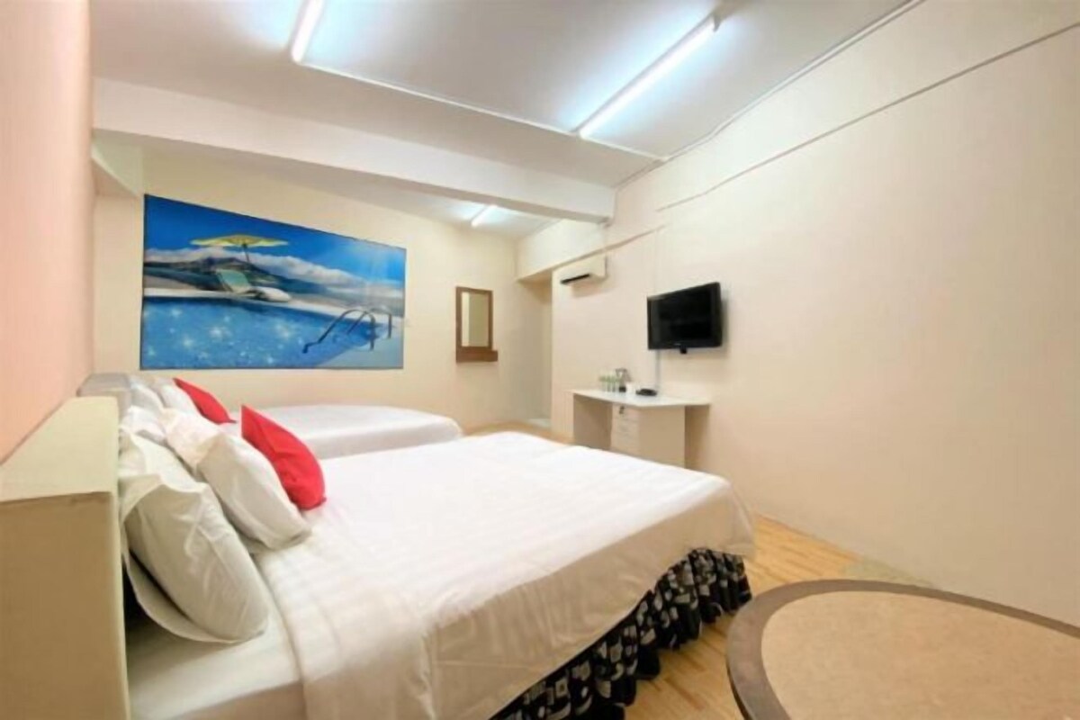 A hotel room with a bed, a television, a painting, and a small table.