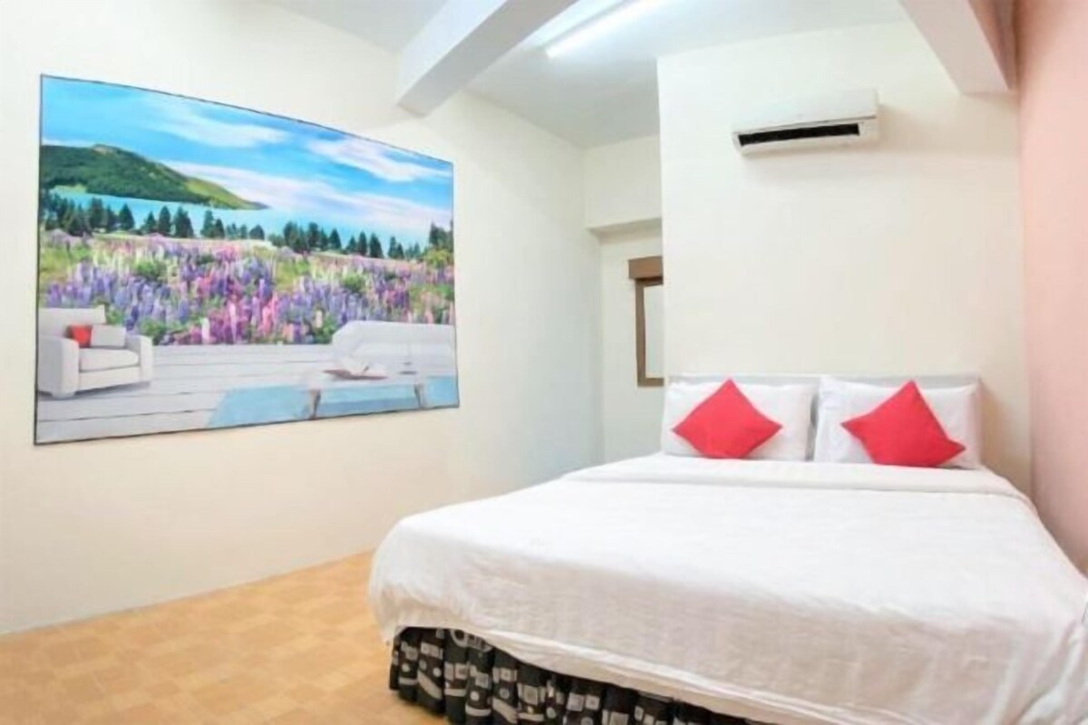 A bedroom with a bed, white bedding, and a painting of a landscape on the wall.