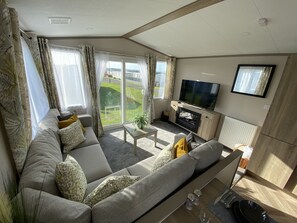 Un salon moderne doté d’un grand canapé, d’un téléviseur à écran plat et d’une porte-fenêtre coulissante donnant sur un balcon.