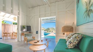 A spacious living area with a green sofa, a wooden coffee table, a TV, and a view of the sea. - Villa Rackam, balcony on the Baie des Saintes with pool and 300m from beaches (Terre-de-Haut)