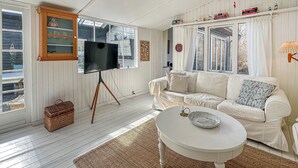 A living room with a white sofa, a television on a tripod stand, a small table with a bowl, and a wicker basket. - Amazing home in Gilleleje with sauna (Gilleleje)