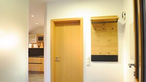 Een gang met een houten deur, een bankje en een wandplank.