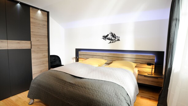 Een moderne slaapkamer met een bed, houten vloer en een kunstwerk aan de muur.